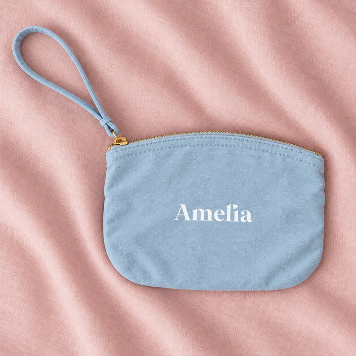 Blue canvas personalised bridesmaid wristlet pouch with the name Amelia, on pink linen