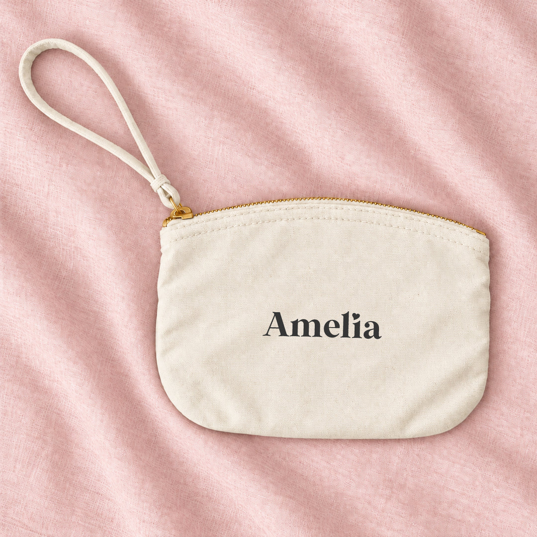 Natural cream canvas personalised bridesmaid wristlet pouch with the name Amelia, on blush linen