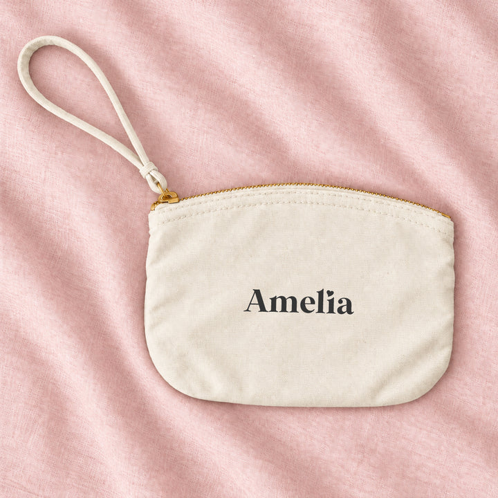Natural cream canvas personalised bridesmaid wristlet pouch with the name Amelia, on blush linen