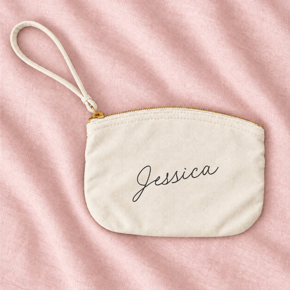 Natural cream canvas personalised bridesmaid wristlet pouch with the name Jessica in script, on blush linen