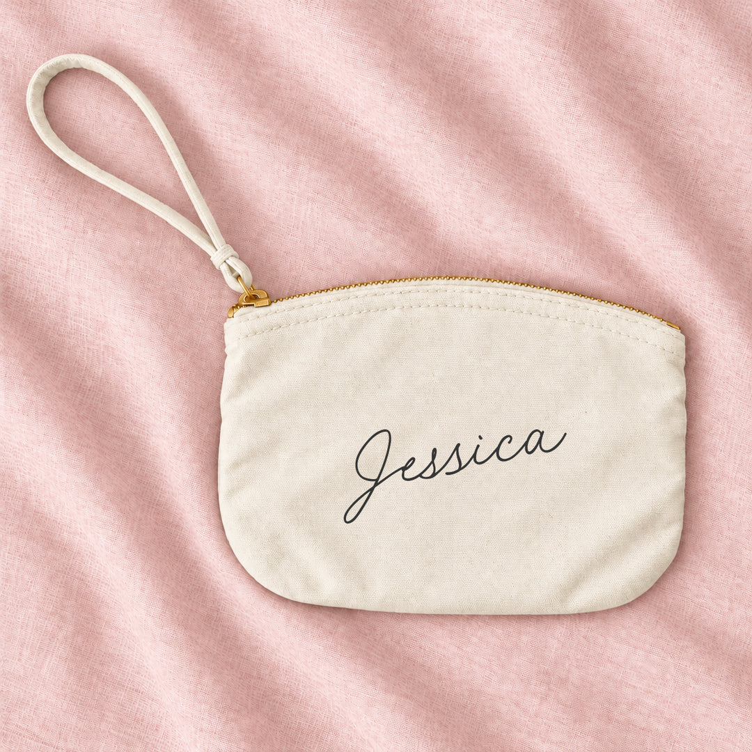 Natural cream canvas personalised bridesmaid wristlet pouch with the name Jessica in script, on blush linen