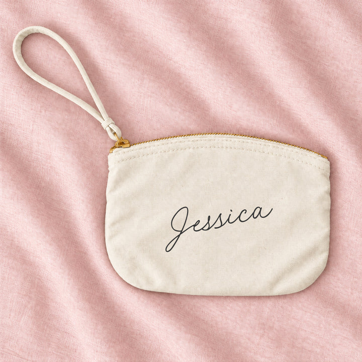 Natural cream canvas personalised bridesmaid wristlet pouch with the name Jessica in script, on blush linen