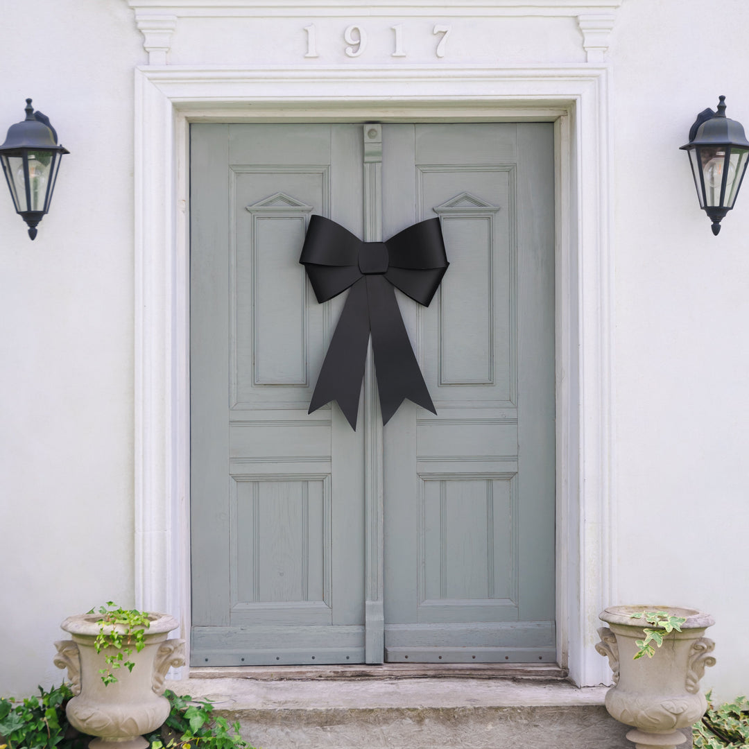 Gray door with a black bow, flanked by two black lanterns on a white wall.
