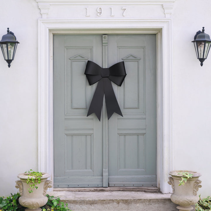 Gray door with a black bow, flanked by two black lanterns on a white wall.