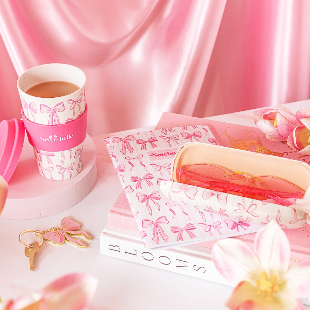 Pink and white coffee cup with matching accessories on a pink fabric background