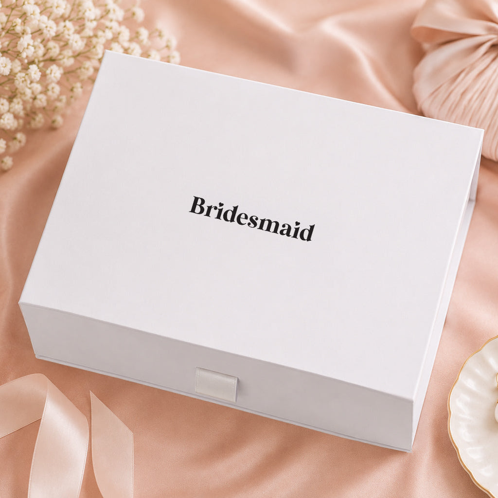 White box labeled 'Bridesmaid' on a pink satin surface with decorative elements.