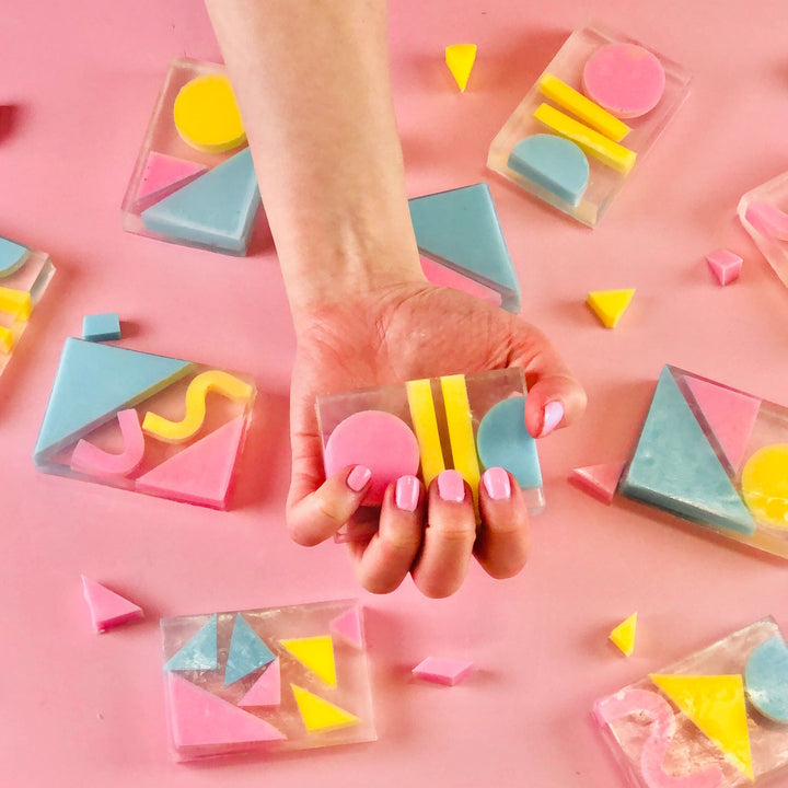 Hand holding a clear cube with colorful geometric shapes on a pink background