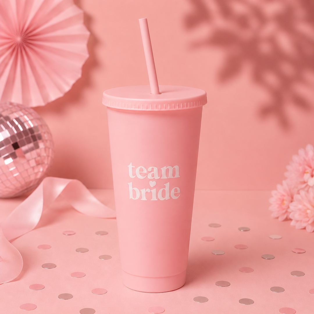 Pink tumbler with 'team bride' text on a polka dot surface with decorative items.
