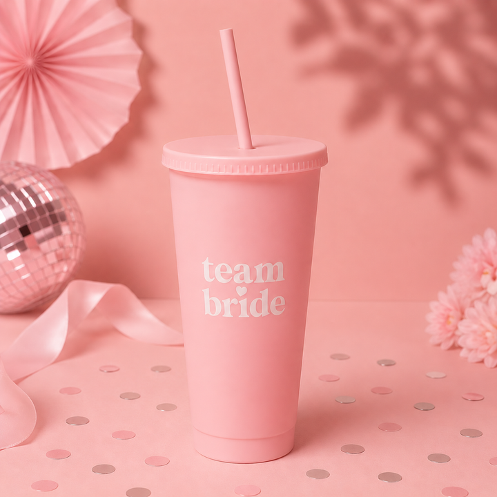 Pink tumbler with 'team bride' text on a polka dot surface with decorative items.